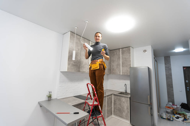electrician, a male electrician is standing on the stairs holding wiring in his hands and stripping, repairing light at home, repair work, call master, electrician man repairing light - Foto, afbeelding