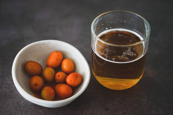 Cuenco de aceitunas especiadas junto con un vaso de cerveza fria  sobre un fondo de madera - Фото, зображення
