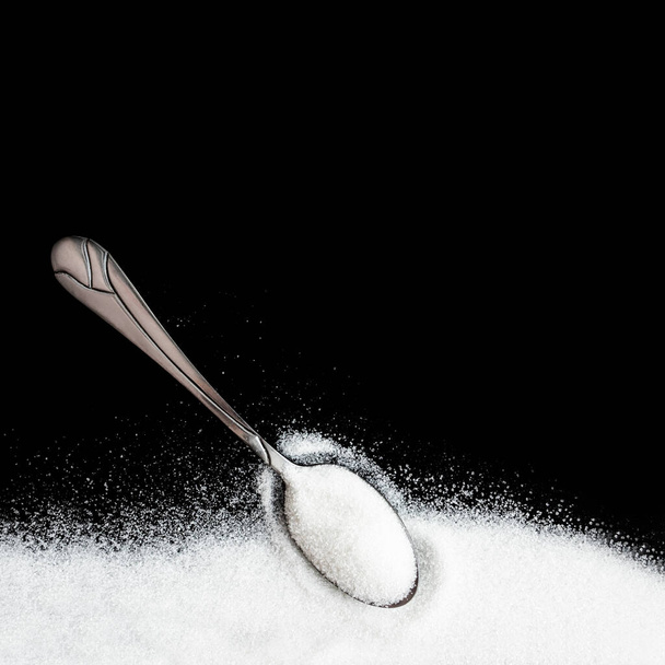 a cukor, a fekete-fehér cukor előnyeinek és ártalmainak fogalma.hiperglikémia, hipoglikémia. Cukor fekete alapon, fém kanállal, felülnézetből, hely a szövegnek, fehér cukor ártalom vagy előny, édes élet.granulált cukor. - Fotó, kép
