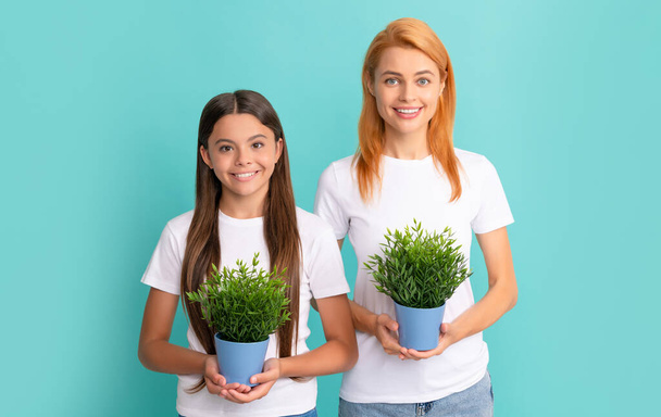 Happy woman mother and adopted daugher child smile holding pot plants blue background, fostering - Photo, Image