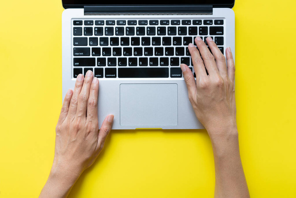женщина, работающая на ноутбуке, сидя в креативном офисе или кафе на желтом фоне стола - Фото, изображение