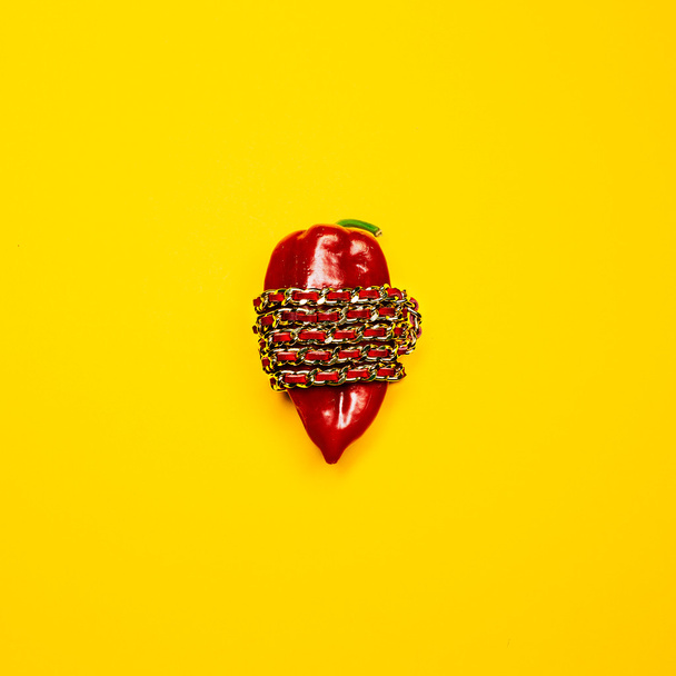 Conceptual fashion photography. Bright red pepper wrapped gold chain on a yellow background. - Zdjęcie, obraz