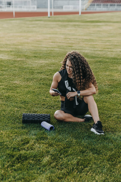 Női sportoló ül a gyepen egy stadionban, és gépel - Fotó, kép