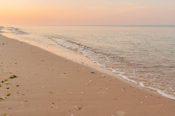 日没時には海や海の砂浜で波のサーフィン。ビーチが空の間の日没の間に背景に砂浜と日光の海や海の波の白い泡. - 写真・画像