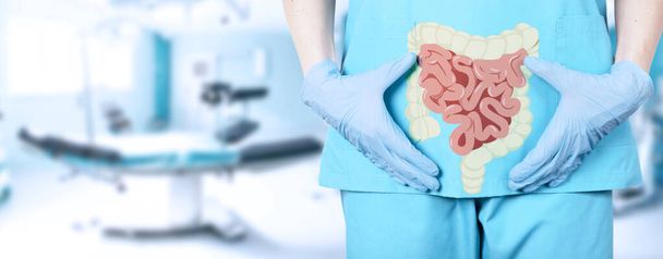 Close-up of a female surgeon doctor in a medical uniform and an icon of the intestine with a large intestine on the background of the operating table in the hospital, soft blurred background. High quality photo - Fotoğraf, Görsel