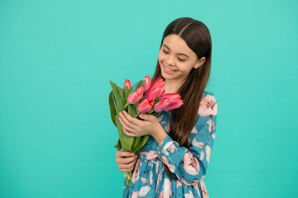 smiling teen girl with spring bouquet on blue background. floral present. - Фото, зображення