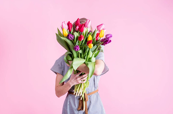 International Women's Day. pretty charming brunette young woman dressed yellow clothes holding tulip bunch isolated pink color background - Zdjęcie, obraz