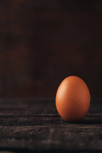 Hnědé kuřecí vejce stojí na tmavém pozadí. Soustřeď se na produkt. Univerzální jídlo a přísada pro vaření nebo pečení. - Fotografie, Obrázek