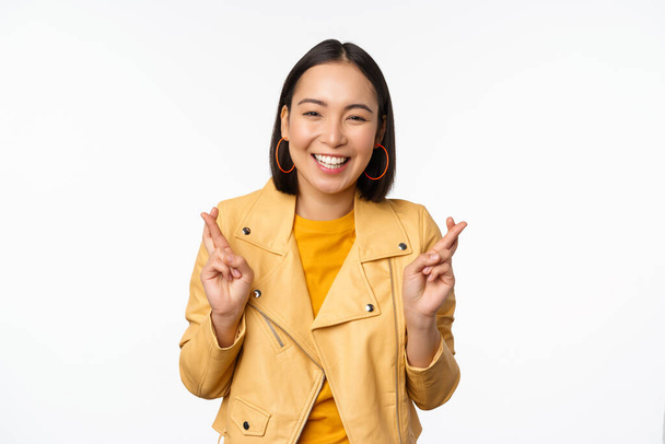 Portrait of excited asian woman looks hopeful, wishing, praying or begging, waiting for news, standing over white background, smiling enthusiastic - Photo, Image