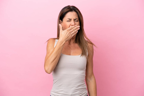 Mulher caucasiana de meia idade isolada em fundo rosa bocejando e cobrindo a boca aberta larga com a mão - Foto, Imagem