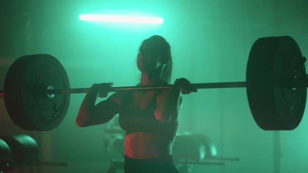 スローモーション:アスレティック・ビューティフル・ウーマンはジムのバーベルでデッドリフトをオーバーヘッドします。女性のプロのボディービルダーワークアウト本物のスポーツトレーニング施設での重量リフトの演習. - 映像、動画