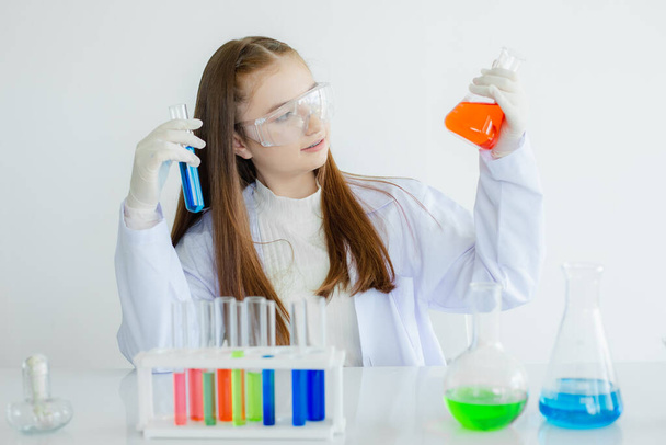 Μαθητές φυσικής παιδιών μελετούν πειράματα υγρής χημείας σε λευκό εργαστηριακό χώρο. μαθήτρια που κρατά δοκιμαστικό σωλήνα με την εκμάθηση της βιοτεχνολογίας. cocept επιστημονικής εκπαίδευσης. - Φωτογραφία, εικόνα