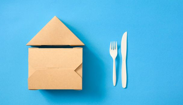 Dos contenedores de comida rápida ecológicos y un tenedor con un cuchillo sobre un fondo de papel azul. Los contenedores se apilan en forma de casa. Colocación plana, espacio de copia, maqueta. - Foto, Imagen