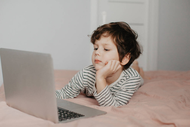 Little boy lie in the bedroom on the bed and look at the laptop - Foto, Bild