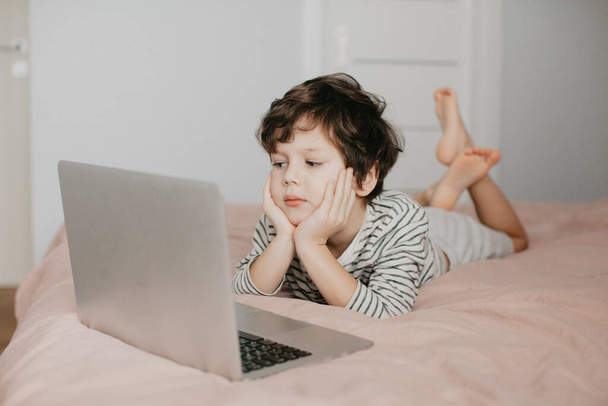 Little boy lie in the bedroom on the bed and look at the laptop - Zdjęcie, obraz