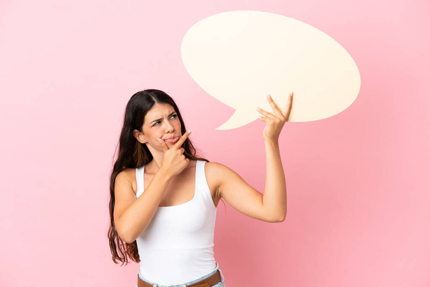 Молодая белая женщина изолирована на розовом фоне, держит пустой пузырь речи и думает: - Фото, изображение