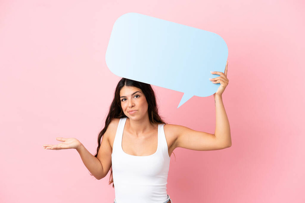 Young caucasian woman isolated on pink background holding an empty speech bubble and having doubts - Foto, Imagem