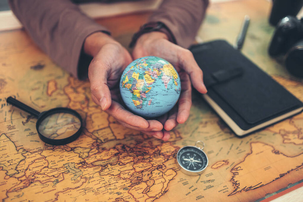Globe, whole world in hands and compass, magnifying glass and book on route map on the table. Travel , Adventure and Discovery concept. - Фото, изображение