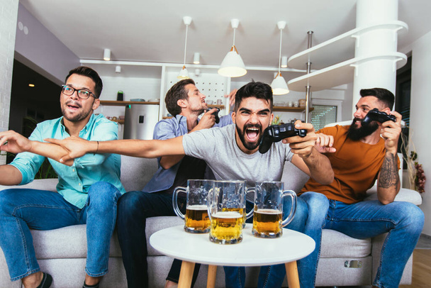 amistad, tecnología y concepto de ocio - amigos varones sonrientes con mandos y cerveza jugando videojuegos en casa  - Foto, imagen