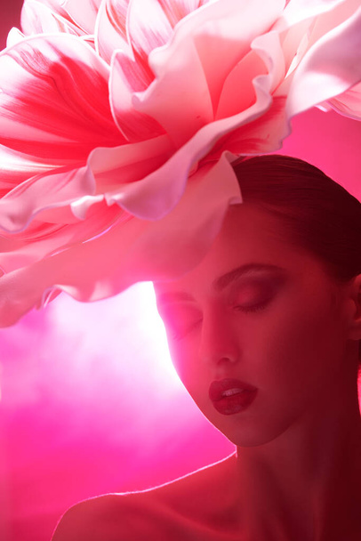 Perfumery and women's beauty.  Close up portrait of an adorable  brunette girl with a large delicate peony flower on her head. Makeup and cosmetics. - 写真・画像