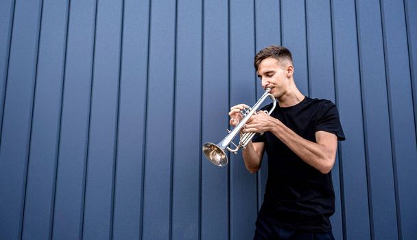 Young street musician playing the trumpet near the big blue wall - Photo, Image