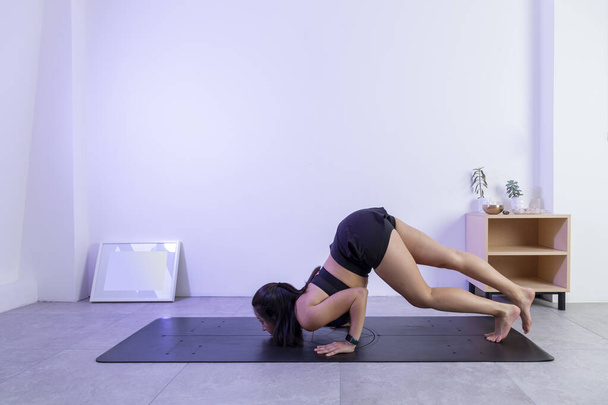 Proceso de posar, de una mujer haciendo la pose de escorpión en un estudio de yoga, usando ropa deportiva. - Foto, Imagen