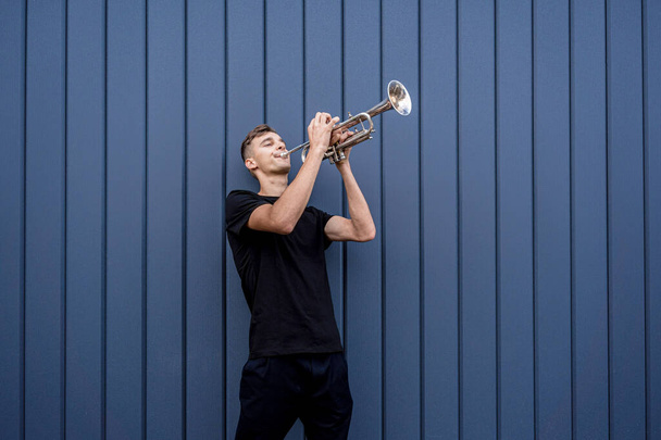 Young street musician playing the trumpet near the big blue wall - Foto, Imagen