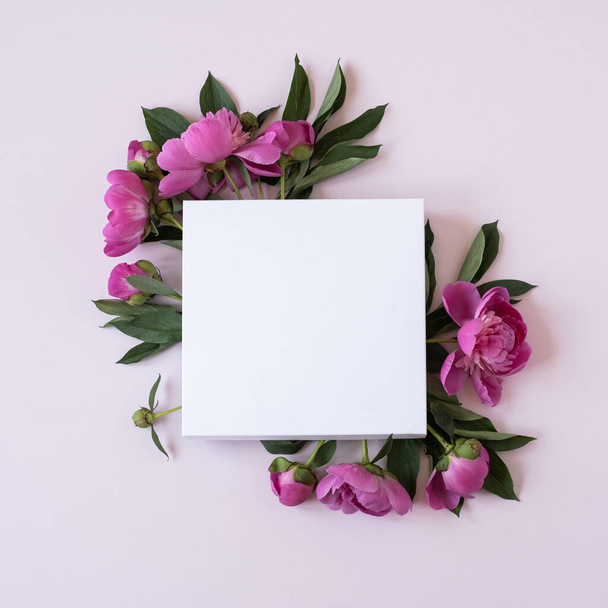 Wreath made of elegant pink peonies flowers with blank mockup copy space paper sheet on pastel pink background. Flat lay, top view brand, blog, website, social media template - Photo, image
