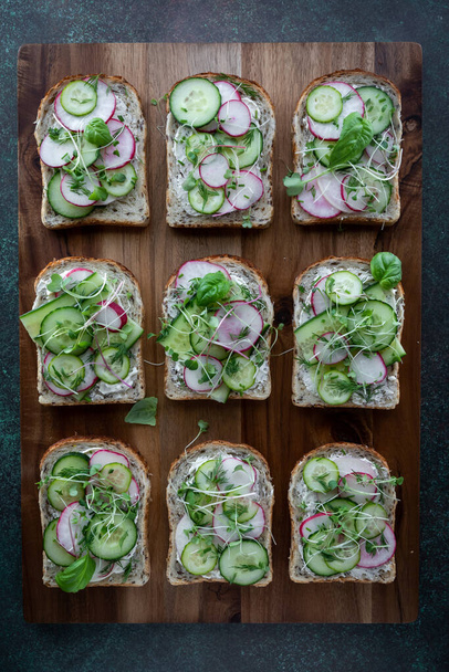 Top down view of cucumber and radish open faced sandwiches on a wooden board. - 写真・画像