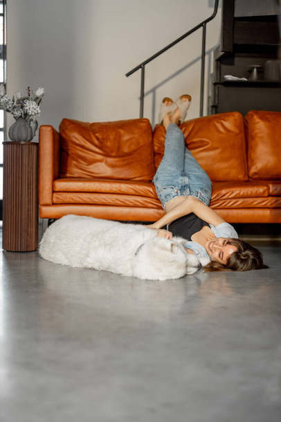 Γυναίκα ξαπλωμένη χαλαρή με το αξιολάτρευτο σκυλί της στο πάτωμα κοντά στον καναπέ στο σπίτι - Φωτογραφία, εικόνα