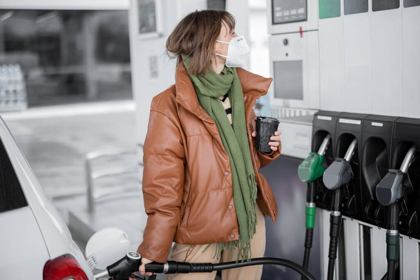 Nainen naamiossa tankkaamassa autoa bensiinillä huoltoasemalla - Valokuva, kuva