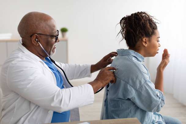 Fekete férfi orvos ellenőrzi a női beteg leheletét - Fotó, kép