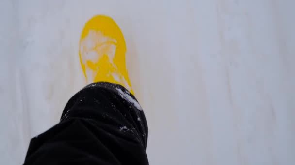 Humano en pantalones oscuros y botas de caucho amarillo cálido camina sobre nieve blanca en invierno, vista en primera persona desde arriba. Imágenes 4K en cámara lenta. - Metraje, vídeo