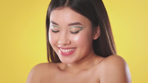 Joven mujer asiática positiva con maquillaje creativo y hombros desnudos sonriendo a la cámara, cámara lenta - Imágenes, Vídeo