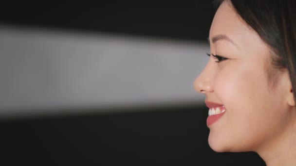Profil portrét pozitivní asijské ženy dívající se stranou na prázdný prostor, černé pozadí s paprskem světla, zpomalený pohyb - Záběry, video