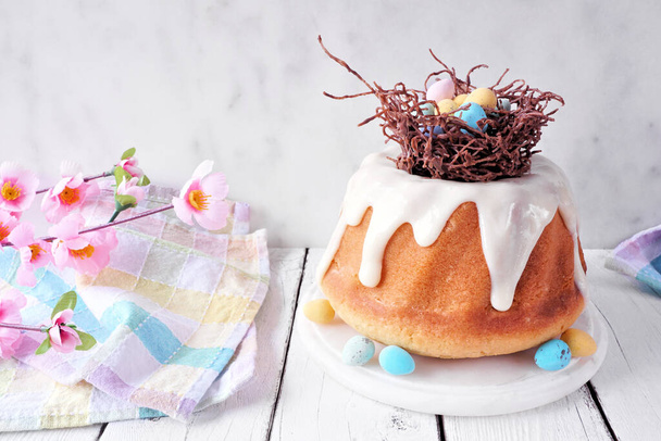 Пасхальный торт с шоколадным гнездом разноцветных шоколадных яиц. Вид сбоку стол сцены на ярком фоне дерева. - Фото, изображение
