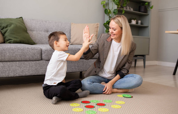 Un petit garçon heureux joue avec sa mère sur le tapis dans la pièce dans un jeu de logique éducatif. Développement précoce de l'intelligence - Photo, image