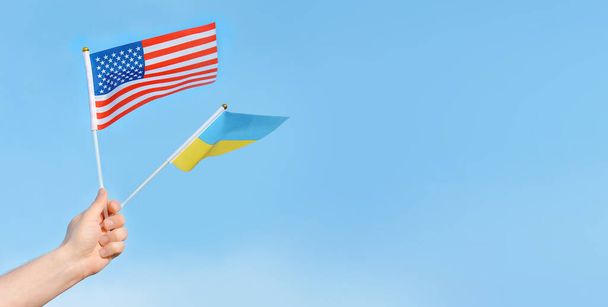 Banderas de los EE.UU., Ucrania en la mano de un hombre contra el cielo azul.Copiar el espacio para el texto - Foto, Imagen