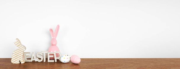 Decoración de Pascua en un estante de madera. Signo de Pascua, huevos y conejitos de vidrio modernos contra una pancarta de pared blanca. Copiar espacio. - Foto, Imagen