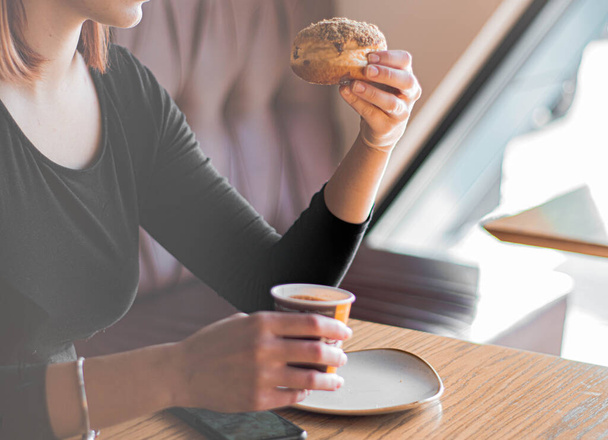 Woman in restaurant holds tasty donut in hand - Foto, afbeelding