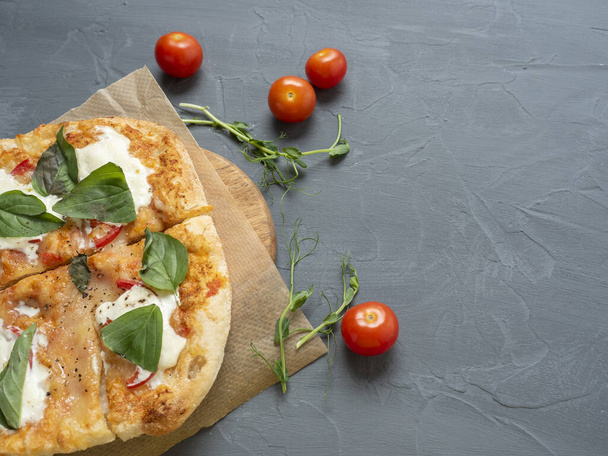 Close-up of delicious fresh crispy Roman pizza with cheese and herbs on a gray background. Fresh ripe tomatoes are nearby. Craft paper. Top view, flat lay, copy space - Photo, Image