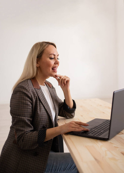 uma fonoaudióloga feminina em uma jaqueta se senta a uma mesa e conduz remotamente uma lição com um laptop em um fundo branco com um lugar para texto - Foto, Imagem