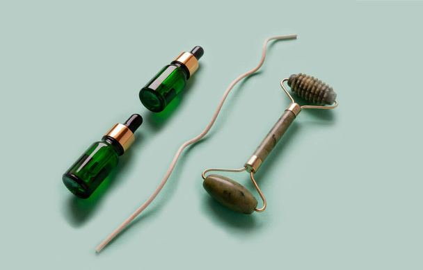 Two cosmetic bottles with dropper and jade face roller massager.  Mockup, copy space, top view on faded green background - Valokuva, kuva