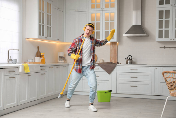 Handsome young man with headphones singing while cleaning kitchen - Foto, immagini