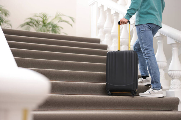 Man with suitcase going up stairs in hotel, closeup - Foto, imagen