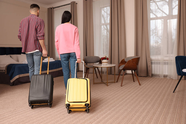 Couple with suitcases walking into hotel room, back view - Photo, Image