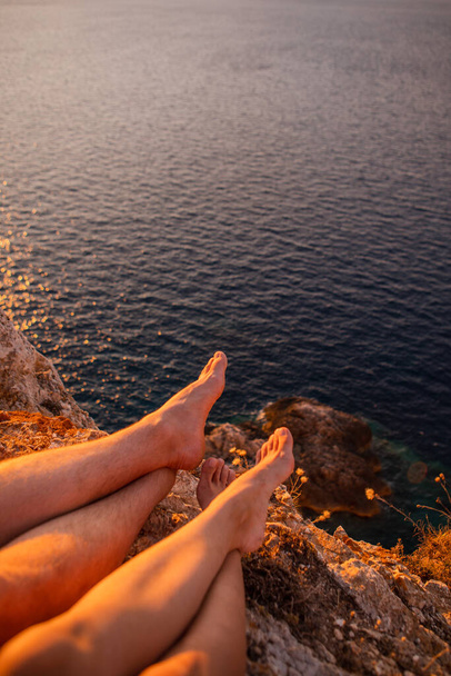 崖の上に座って顔もなく夕日を楽しんでるカップル - 写真・画像