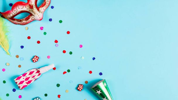 Maškarní maska, barevné konfety, píšťalka a píšťalka ležely nalevo na světle modrém pozadí s kopírovacím prostorem napravo. Mardi gras prázdninový koncept. - Fotografie, Obrázek