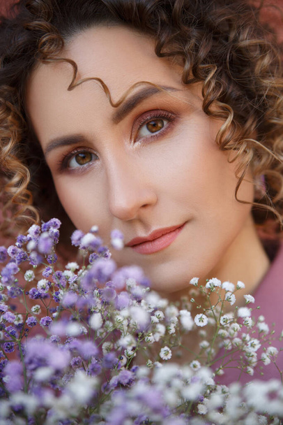 Portrait of a lovely girl with curls with a bouquet of gypsophila. - Foto, immagini