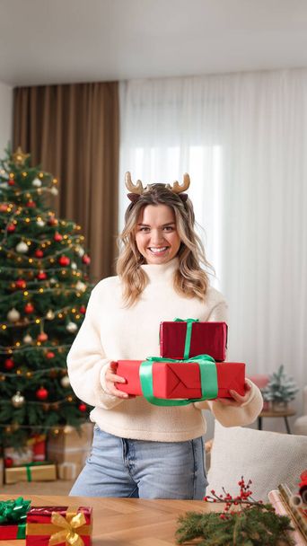 Young woman with beautifully wrapped Christmas gifts at home - Foto, imagen
